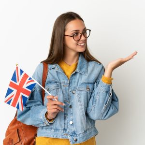 Young hispanic woman holding an United Kingdom flag over isolated white background extending hands to the side for inviting to come Young hispanic woman holding an United Kingdom flag over isolated white background extending hands to the side for inviting to come